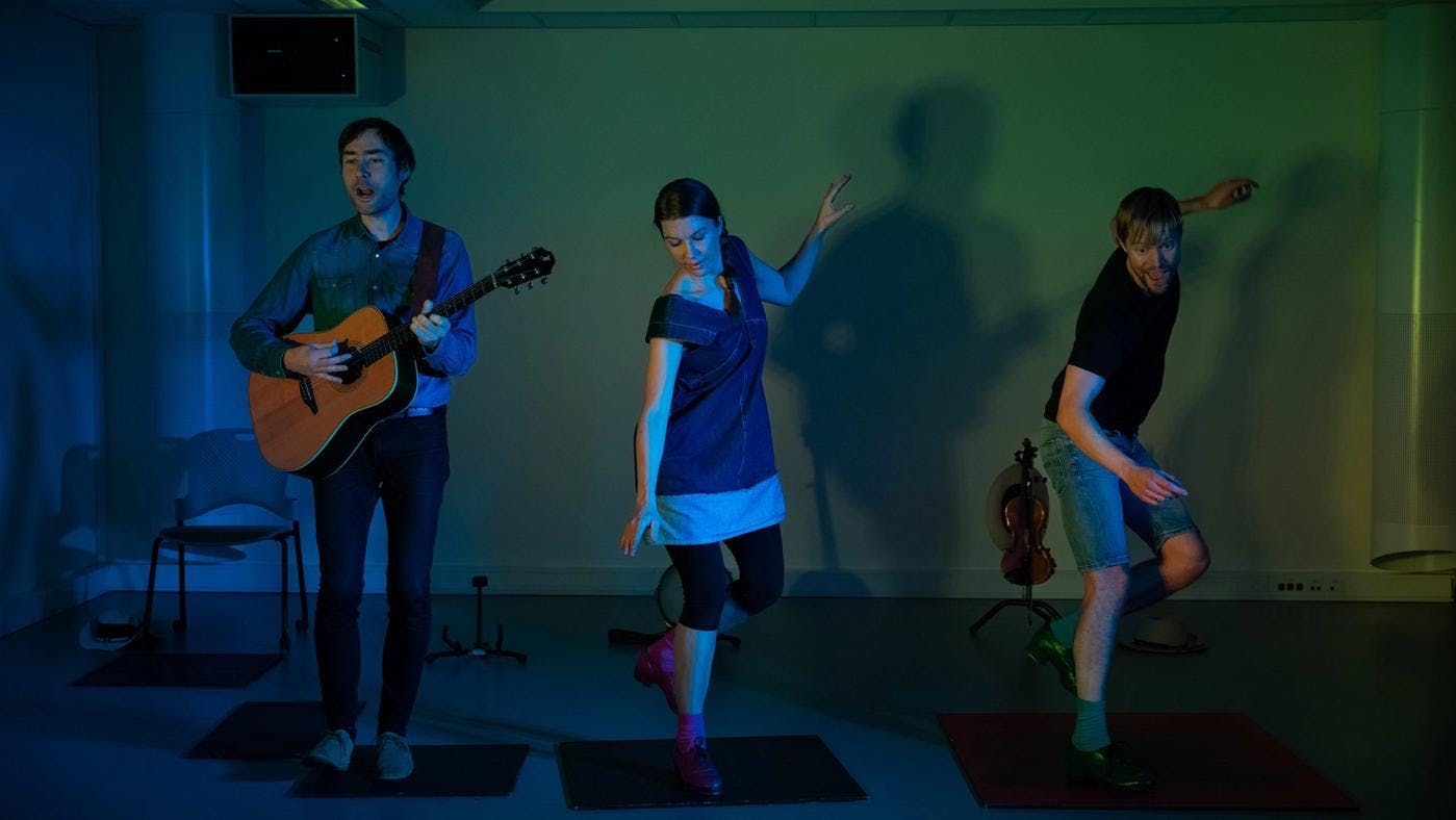 Three performers singing, dancing and playing guitar