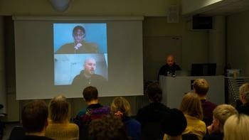 An actor stands in front of a projected view of a video conference 
